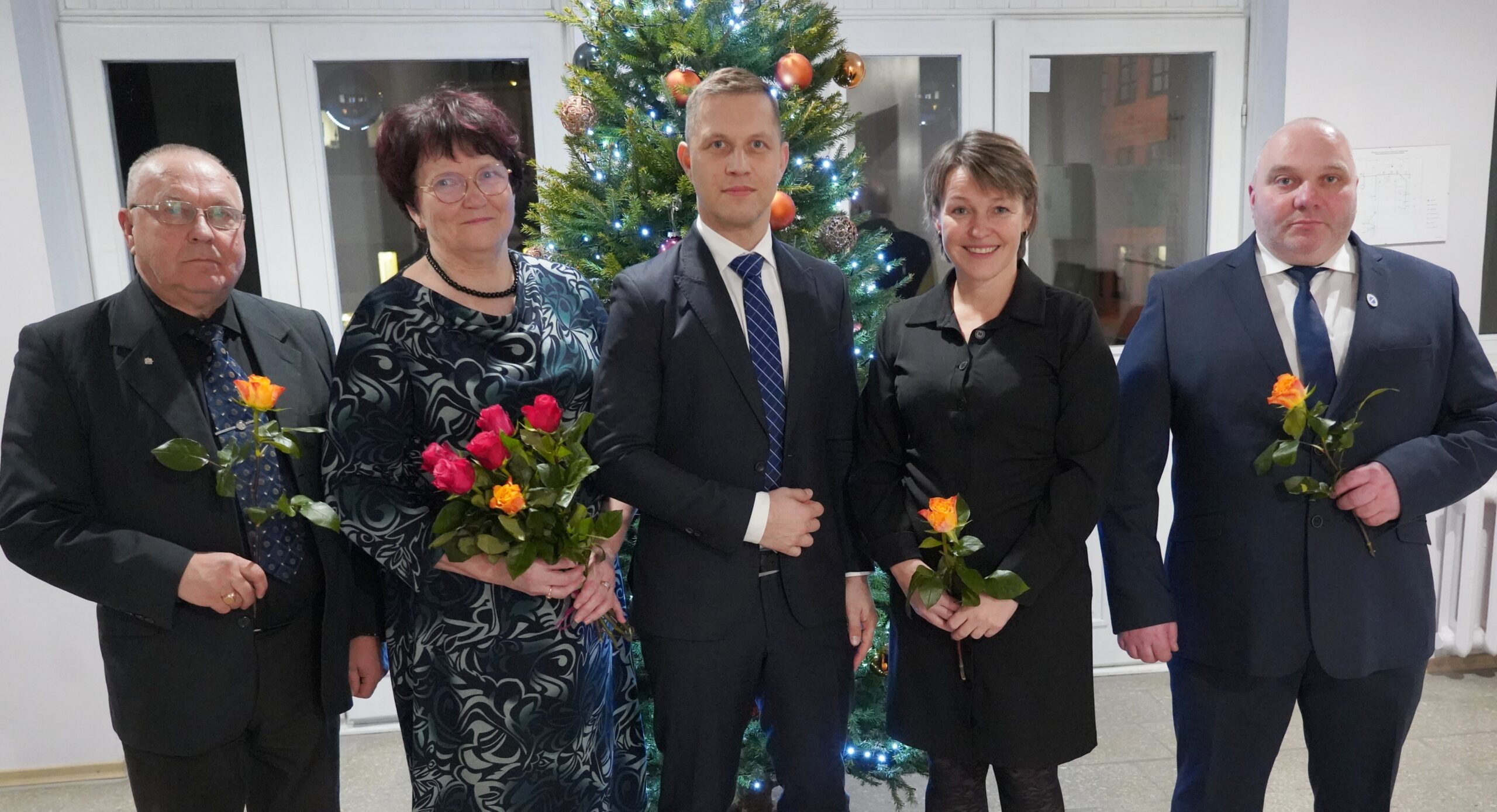 Uus Jõgeva vallavalitsus: Vello Lukk, Helle Kajaste, Karro Külanurm, Kristi Klaos ja Kalle Kabrits. Pildilt puudub Inna Paulus. Uus Jõgeva vallavalitsuse koosseis seisab jõulupuuga taustal. Pildil on viis inimest lilledega käes.